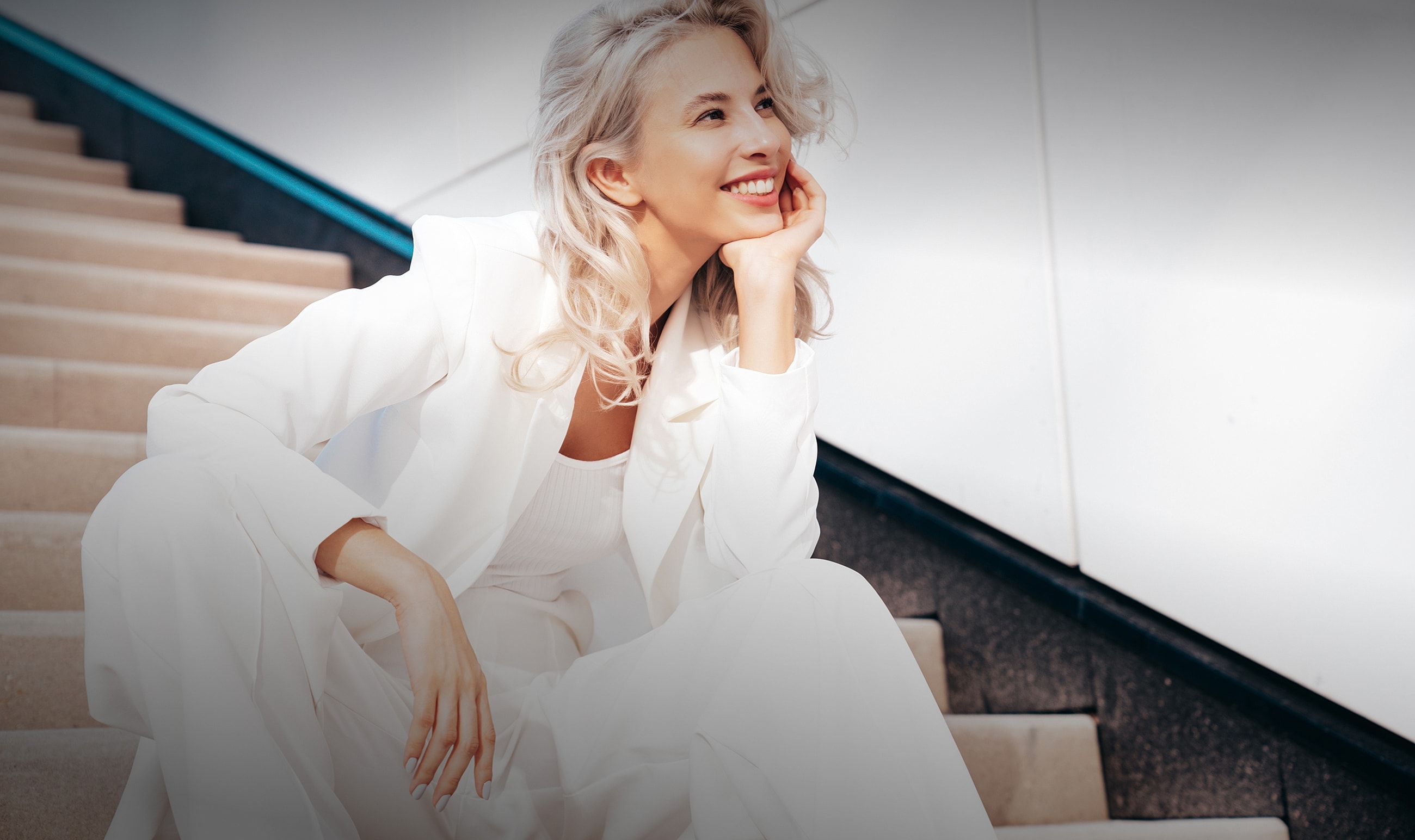 Smiling woman in all-white outfit sitting outdoors.