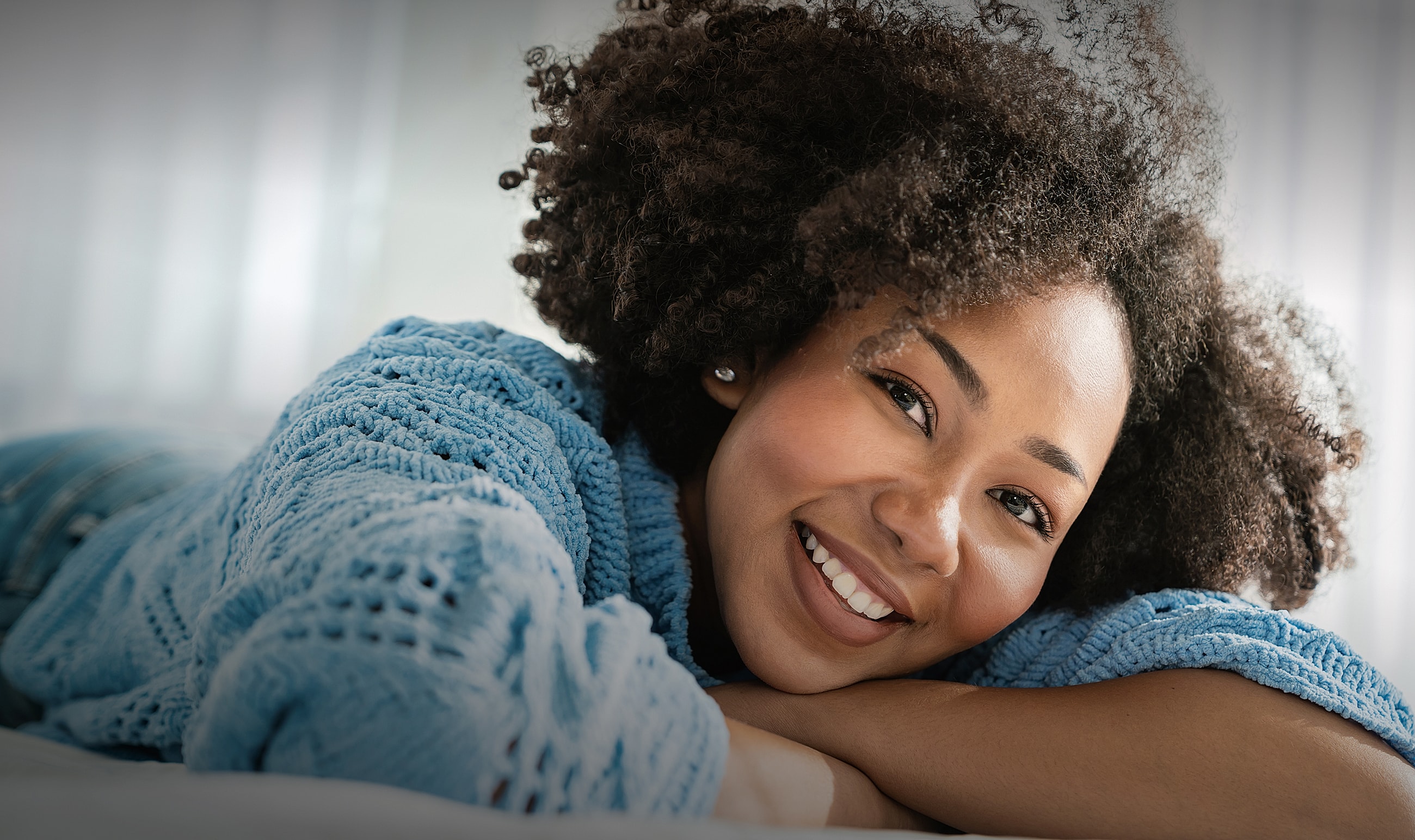 Smiling person in cozy blue sweater laying down.
